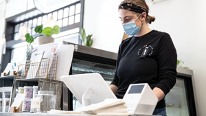 lady in a blue mask swiping a card at a register for customer service training healthy business builder