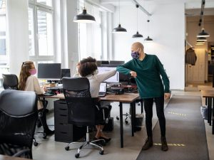 office workers wearing masks elbow bumping at desk on their return to work
