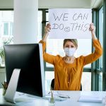 office lady with mask on and a sign "we can do this" return to work